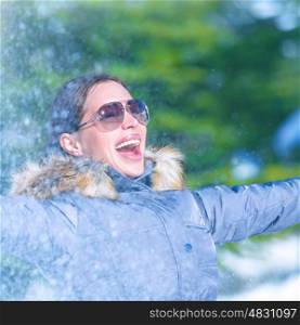Cheerful female in winter park in sunny frosty day, wearing sunglasses, enjoying snowfall, happy wintertime vacation