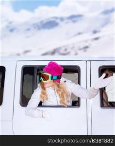 Cheerful female looks out from the car window and waved hand to next auto, wearing goggles, going to luxury ski resort, enjoying winter holidays