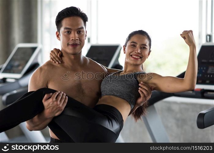 Cheerful fitness Asian couple exercisie treadmills in gym. Handsome man carrying female on his arms and hands. Bodybuilding, healthy lifestyle, and happy relationship concept.
