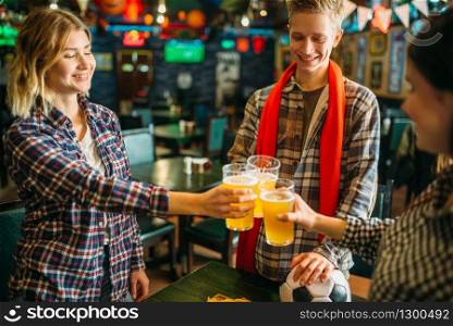 Cheerful football fans raise their glasses with light beer in sports bar. Tv broadcasting, young friends celebrates win of the favorite team, success game celebration in pub