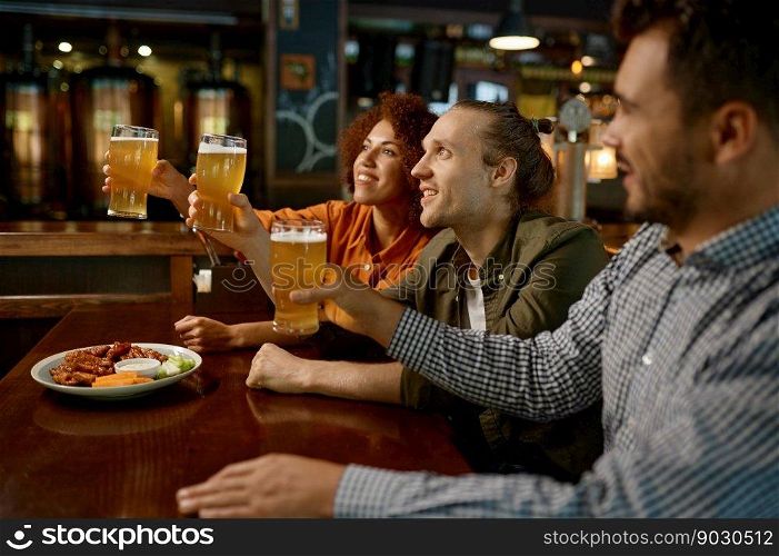 Cheerful friends drinking draft beer at bar table in sports pub. Group of young people with raising beer glasses looking at camera. Cheerful friends drinking draft beer at bar table in pub