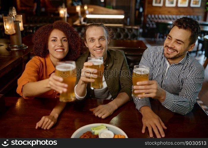 Cheerful friends drinking draft beer at bar table in sports pub. Group of young people with raising beer glasses looking at camera. Cheerful friends drinking draft beer at bar table in pub