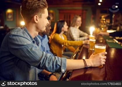Cheerful friends drinks beer at the counter in bar. Group of people relax in pub, night lifestyle, friendship, event celebration. Cheerful friends drinks beer at the counter in bar