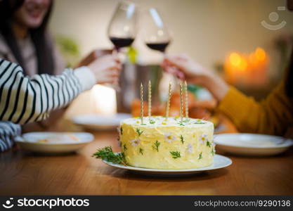 Cheerful friends enjoying home Birthday holiday party. Asian sister cheering drinking red wine celebrating with Birthday cake.