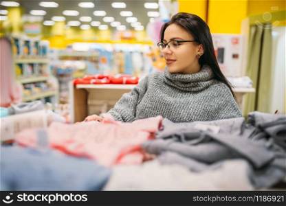 Cheerful future mother in glasses buys childrens clothes in the store for newborns. Pregnant woman in shop of goods for infants