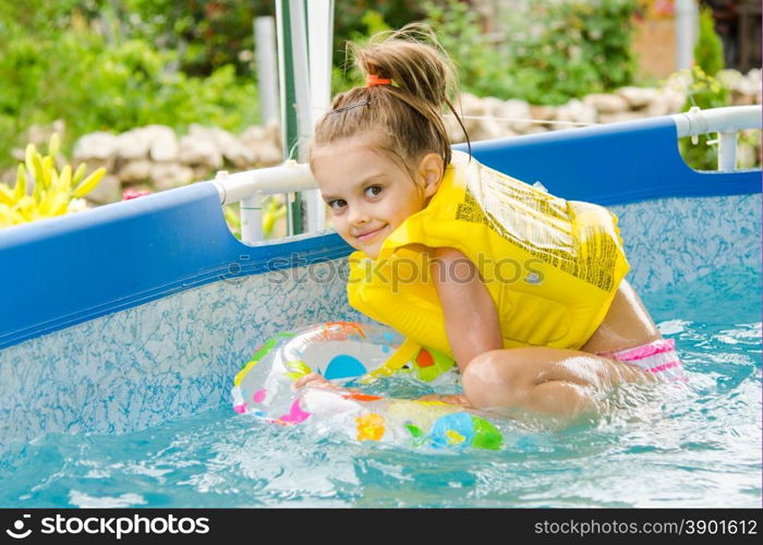 Cheerful girl bathing trying to get into the swimming circle. Six year old girl Europeans bathed in a small suburban pool