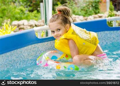 Cheerful girl bathing trying to get into the swimming circle. Six year old girl Europeans bathed in a small suburban pool