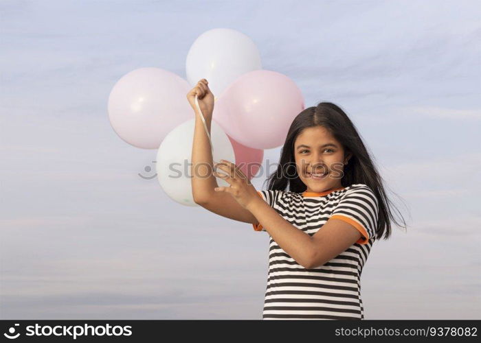 Cheerful girl holding colourful balloons against blue sky