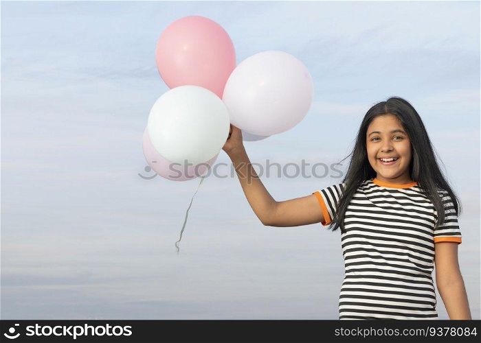 Cheerful girl holding colourful balloons against blue sky