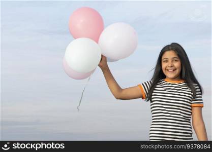 Cheerful girl holding colourful balloons against blue sky