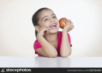Cheerful girl holding fresh red apple against colored background