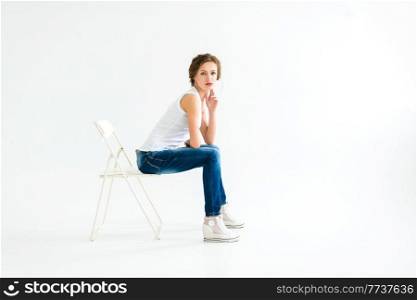 cheerful girl in a white t-shirt and dark blue jeans in the studio on a white background stands, sits, runs