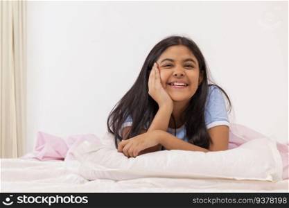Cheerful girl looking at camera with hands on cheek while lying down on bed 