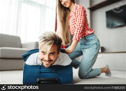 Cheerful girl Packed her husband in a suitcase. Fees on vacation concept. Cheerful girl packed her husband in a suitcase