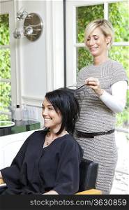 Cheerful hairstylist looking at hair of beautiful woman in beauty salon