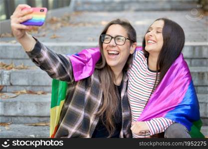 Cheerful happy lesbian couple holding lgbt flag taking a selfie outdoors. High quality photo. Cheerful happy lesbian couple holding lgbt flag taking a selfie outdoors.