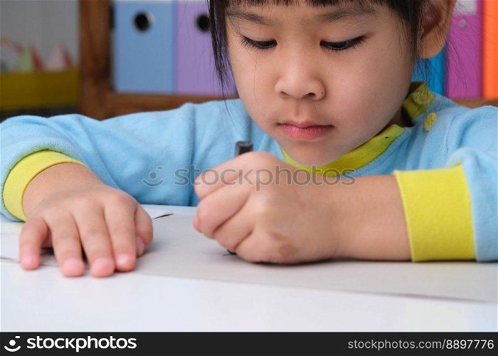 Cheerful happy little girl drawing with crayons on paper sitting at table in her room at home. Creativity and development of fine motor skills.