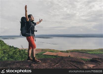 cheerful hiker man gesture raised arms on the edge of cliff, on a top of the rock mountain