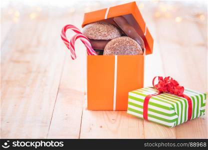 Cheerful image with an orange gift full with gingerbread and candies on a wooden table with light bokeh in the background.