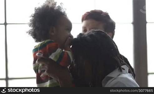Cheerful interracial family and toddler son enjoying great time together at home closeup. Positive african father lifting his little mixed race son up and laughing. Happy mixed race family having fun in domestic interior.