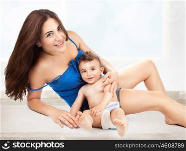 Cheerful joyful mother playing with her adorable son, lying down on the floor at home, enjoying motherhood, happy family life
