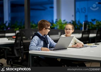 Cheerful little boy in suit talking with young girl in formalwear while sitting at working place. Boy in suit talking girl in formalwear