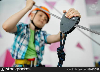 Cheerful little boy on zip line in entertainment center, young climber in helmet. Children having fun in climbing area, kids spend the weekend on playground, happy childhood. Little boy on zip line, young climber in helmet