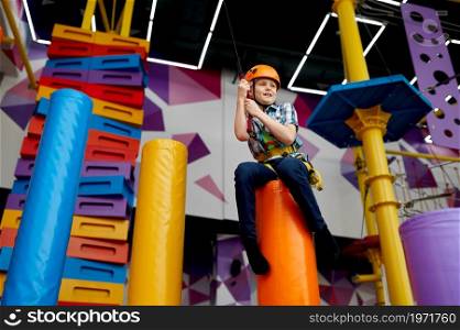 Cheerful little boy on zip line in entertainment center, young climber in helmet. Children having fun in climbing area, kids spend the weekend on playground, happy childhood. Little boy on zip line, young climber in helmet