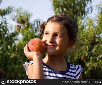 Cheerful little boy playing in the garden holding a peach