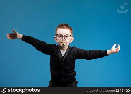 Cheerful little child boy 7s years old in glasses blowing festive pipe at birthday party isolated on blue background. children studio portrait. Childhood lifestyle concept.. Cheerful little child boy 7s years old in glasses blowing festive pipe at birthday party isolated on blue background. children studio portrait. Childhood lifestyle concept