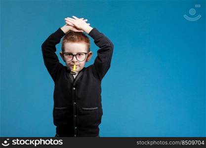 Cheerful little child boy 7s years old in glasses blowing festive pipe at birthday party isolated on blue background. children studio portrait. Childhood lifestyle concept.. Cheerful little child boy 7s years old in glasses blowing festive pipe at birthday party isolated on blue background. children studio portrait. Childhood lifestyle concept