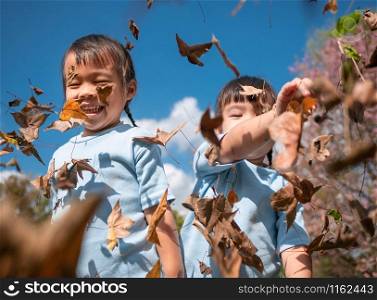 Cheerful little child girl with her sister throwing yellow leaves in autumn park.