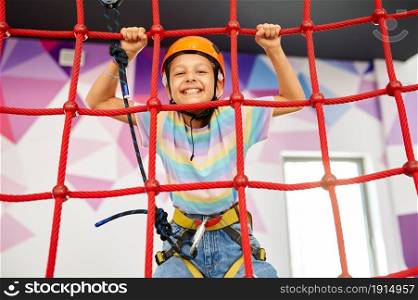 Cheerful little girl holding on to the ropes on zip line in entertainment center. Children having fun in climbing area, kids spend the weekend on playground, happy childhood. Little girl holding on to the ropes, zip line