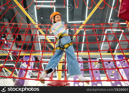 Cheerful little girl holding on to the ropes on zip line in entertainment center. Children having fun in climbing area, kids spend the weekend on playground, childhood. Little girl holding on to the ropes, zip line