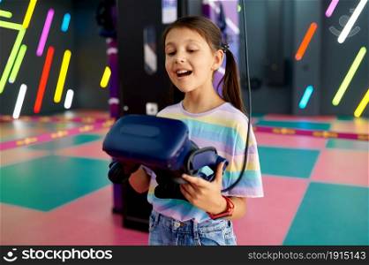 Cheerful little girl holds virtual reality glasses. Kid playing 3d video game in entertainment center. Children having fun in vr, child spend the weekend on playground, happy childhood. Cheerful little girl holds virtual reality glasses