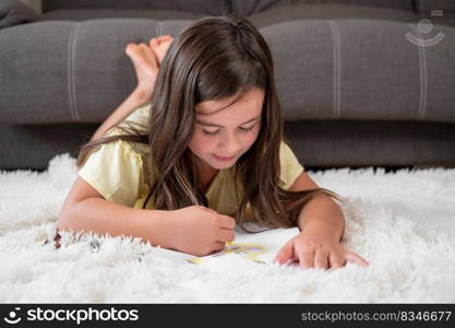 Cheerful little girl lying on the floor drawing . High quality photography. Cheerful little girl lying on the floor drawing.