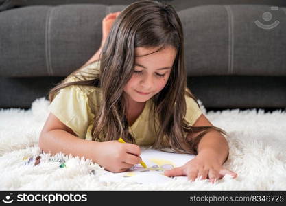 Cheerful little girl lying on the floor drawing . High quality photography. Cheerful little girl lying on the floor drawing.