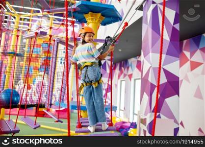 Cheerful little girl on zip line in entertainment center. Children having fun in climbing area, kids spend the weekend on playground, happy childhood. Little girl on zip line in entertainment center