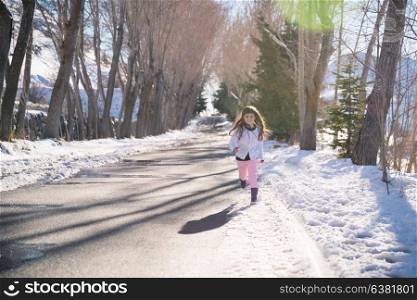 Cheerful little girl running in winter park on sunny day, adorable kid having fun outdoors, enjoying wintertime holidays