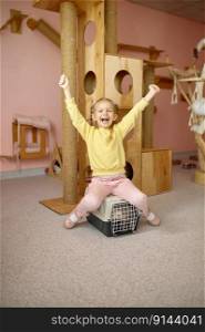 Cheerful little girl sitting on cage with cat over shelter playground. Child enjoying company of having pet and learning responsibility of animal care. Cheerful girl sitting on cage with cat over animal shelter