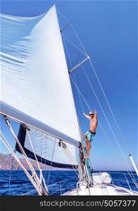 Cheerful man having fun on sailboat, sitting up on the mast of water transport, enjoying active summer vacation, enjoyment and happiness concept