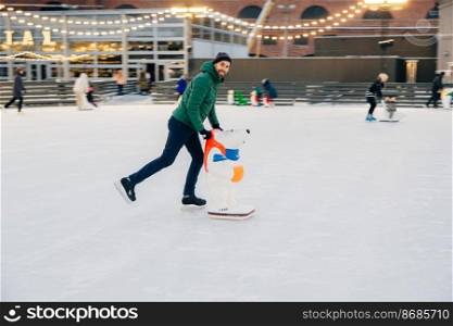 Cheerful man spends free time on skate ring, uses skate aid, learns how to skate, has pleased happy expression, surrounded with people of different age. People, winter, season, hobby concept