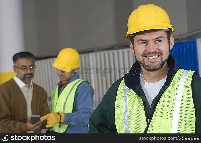 Cheerful man standing in factory colleagues in background