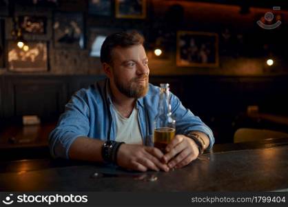 Cheerful man with bottle of beer sitting at the counter in bar. One male person in pub, human emotions, leisure activities, nightlife. Man with bottle of beer sitting at counter in bar