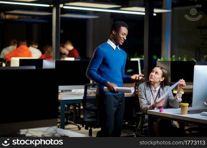 Cheerful managers works in night office. Smiling male and female workers, dark business center interior on background, modern workplace. Cheerful managers works in night office