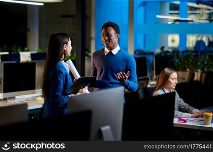 Cheerful managers works in night office. Smiling male and female workers, dark business center interior on background, modern workplace. Cheerful managers works in night office