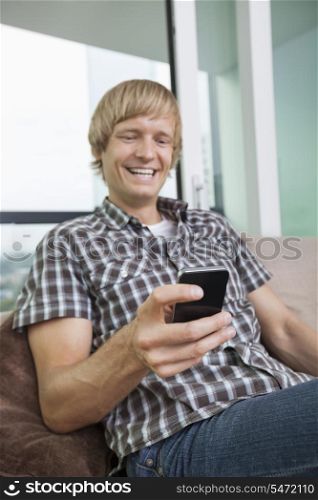Cheerful mid-adult man text messaging on sofa at home