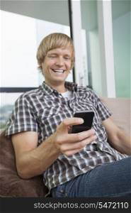 Cheerful mid-adult man text messaging on sofa at home
