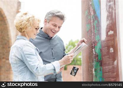 Cheerful middle-aged couple reading map in city