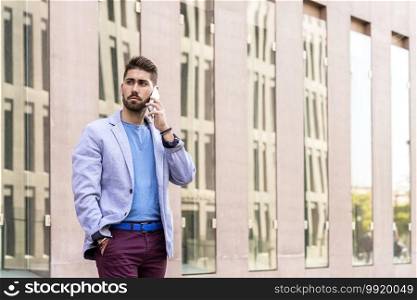 Cheerful modern businessman speaking by phone and smiling while standing outdoors